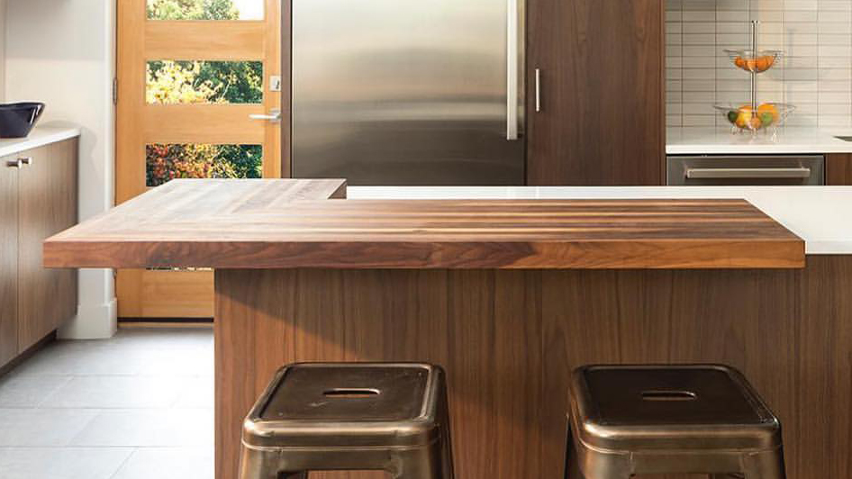 Walnut kitchen island countertop with seating overhang and waterfall support panel in a mid-century modern kitchen.