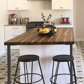 Walnut kitchen island with extended end overhang and bar seating supported by a black steel base.