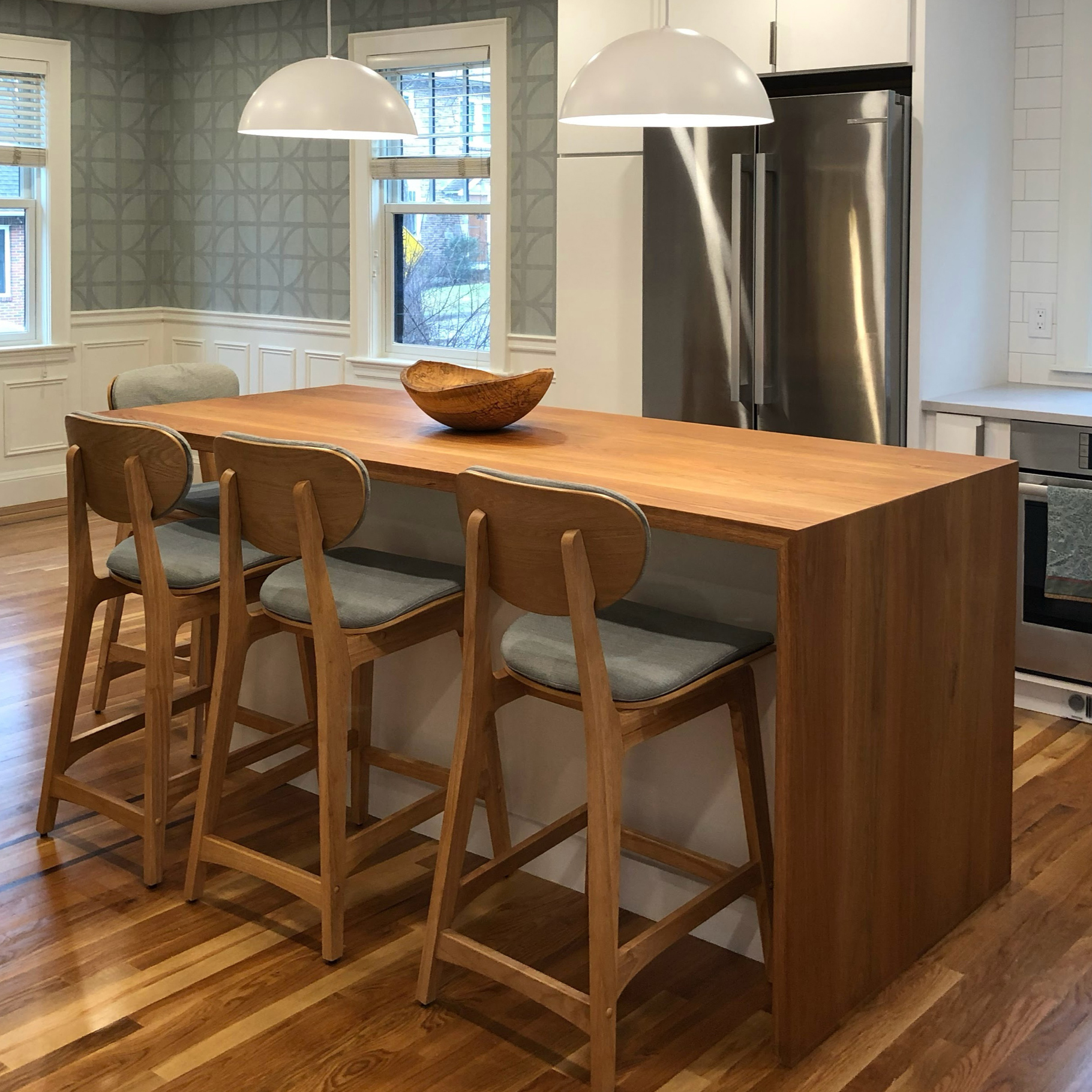 White oak waterfall island with side seating overhang in a modern kitchen interior.